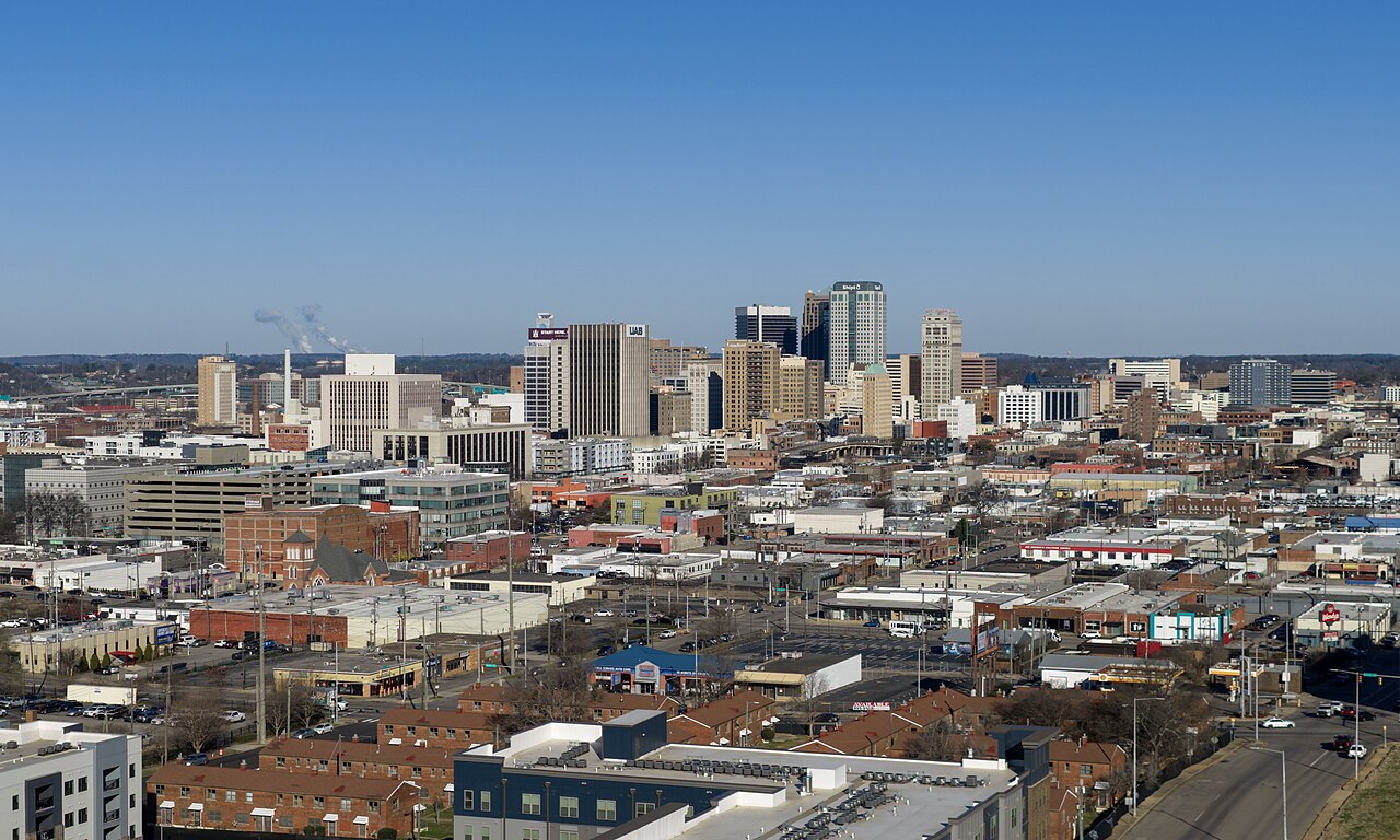 An aerial view of a mid-sized city, low brick blocks in front and a cluster of office towers behind.