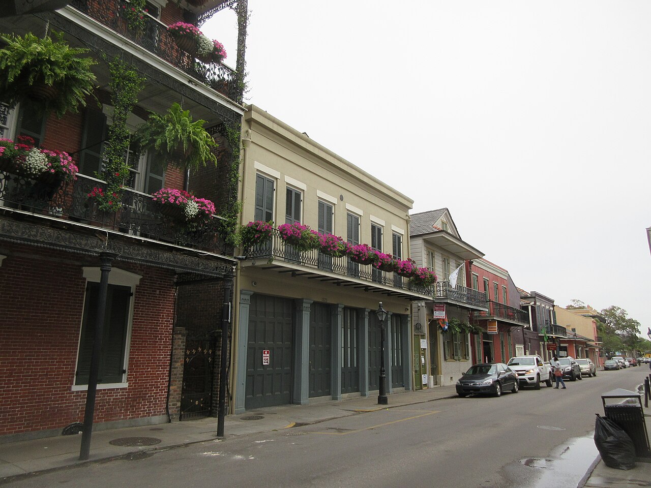 A street of two-storey townhouses with iron balconies hung with flowering plants, cars parked along the kerb.