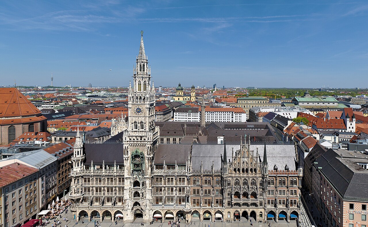 An ornate neo-Gothic town hall with a tall central tower, seen from above with the city's rooftops stretching to the horizon.