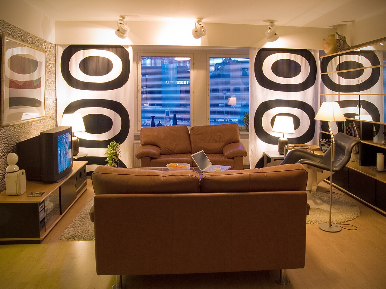Two brown leather sofas face an old television set in a room hung with bold black-and-white patterned curtains.