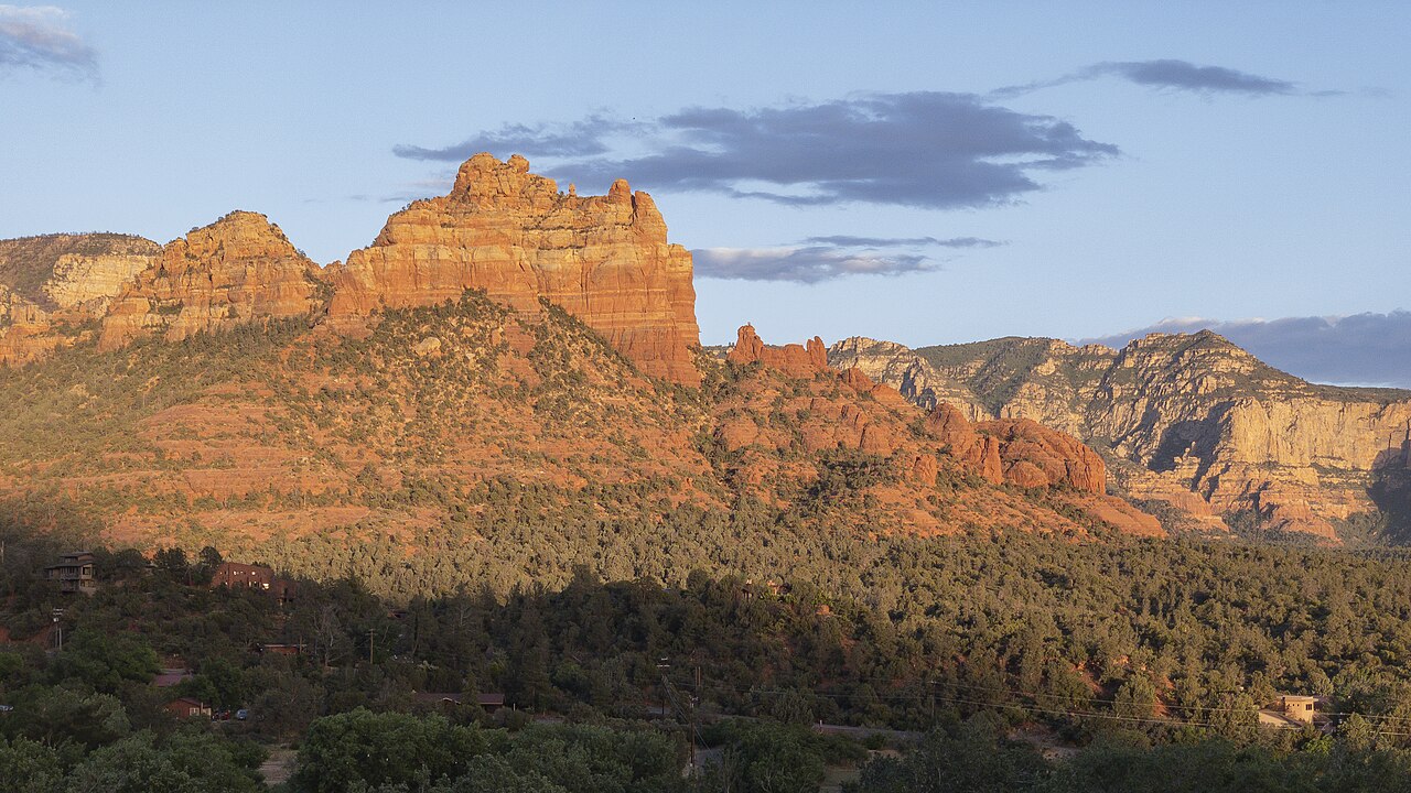 Orange-red sandstone buttes glow in low sunlight above a dark slope of scrub and trees.