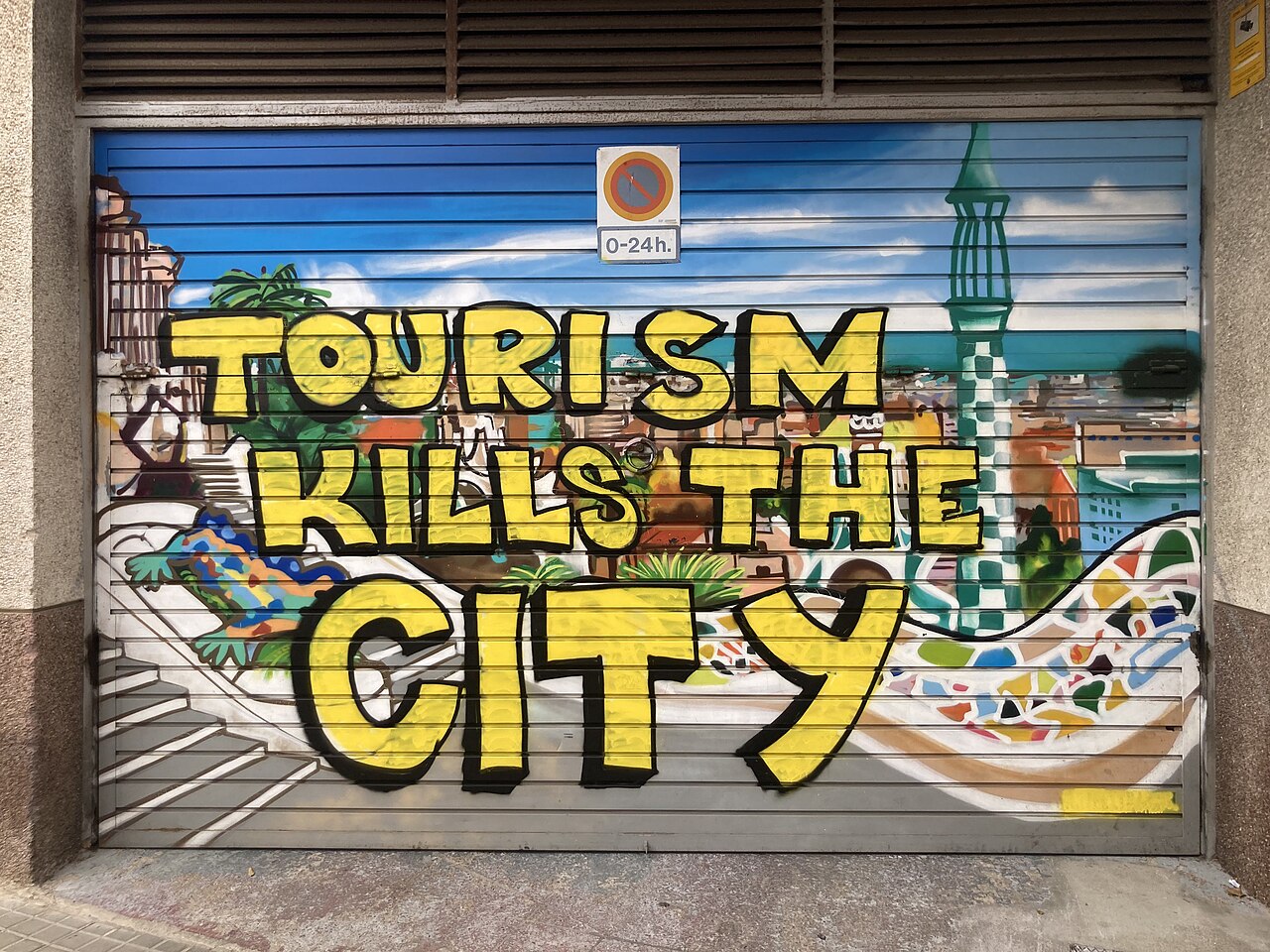 A closed storefront shutter painted with colorful street art and the text Tourism Kills The City.