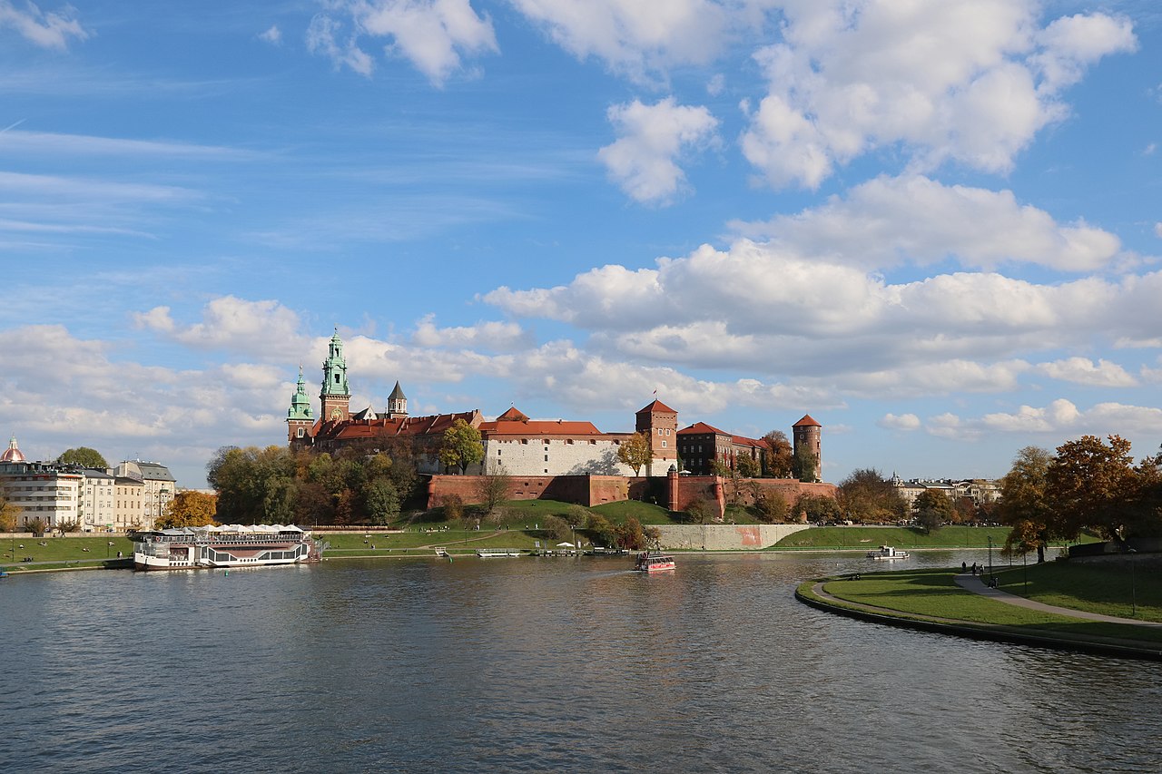 A red-roofed castle and cathedral towers on a hill above a wide river, with a tour boat moored at the bank.