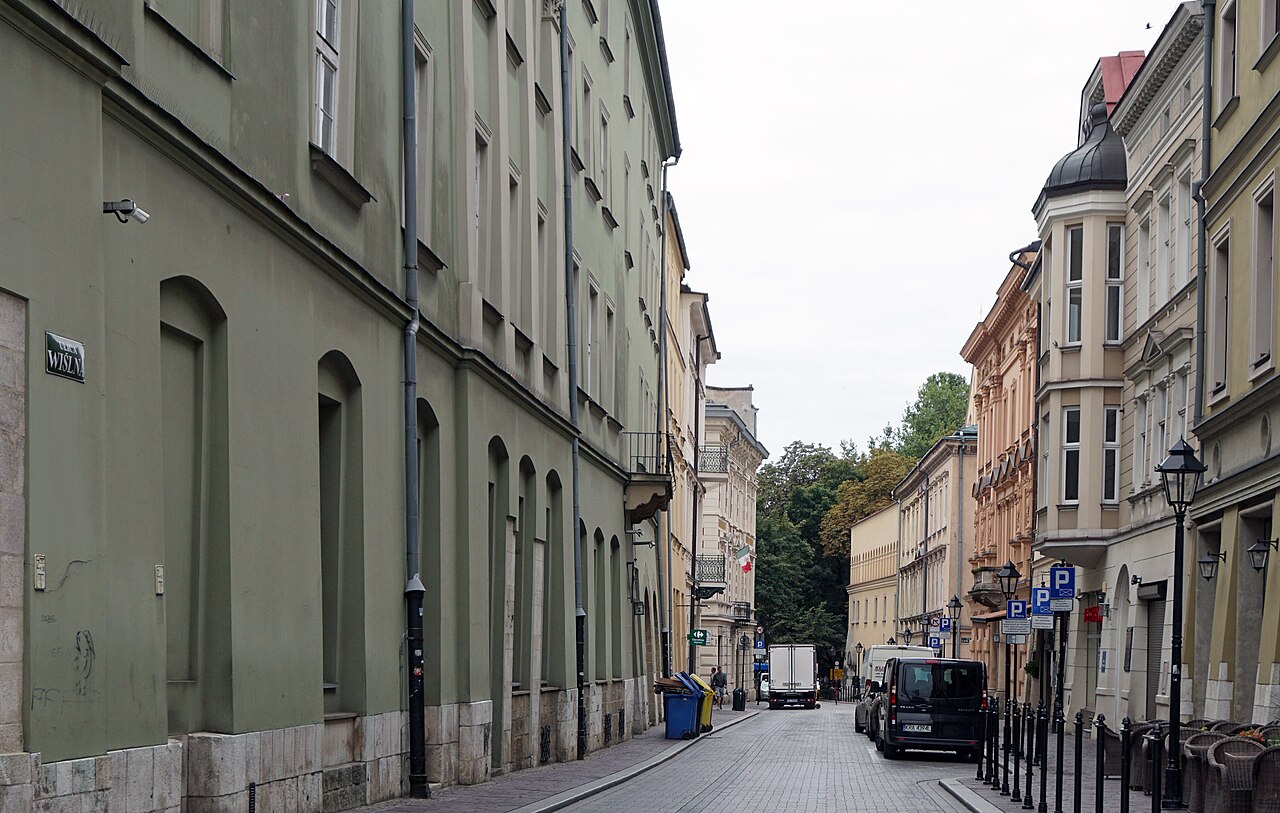 A narrow street lined with old four-storey townhouses in green and cream, with a few parked vehicles.
