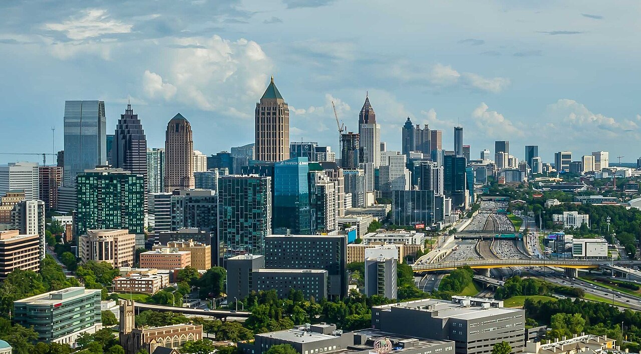 A dense cluster of glass and stone towers seen from above, with highways and trees spreading out toward the horizon.