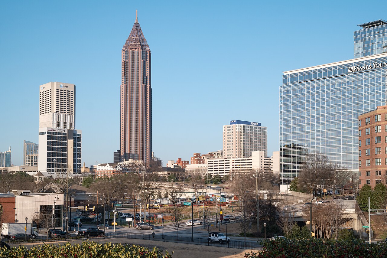 A tall brown tower with a pointed top stands among lower office and hospital buildings under a clear sky.