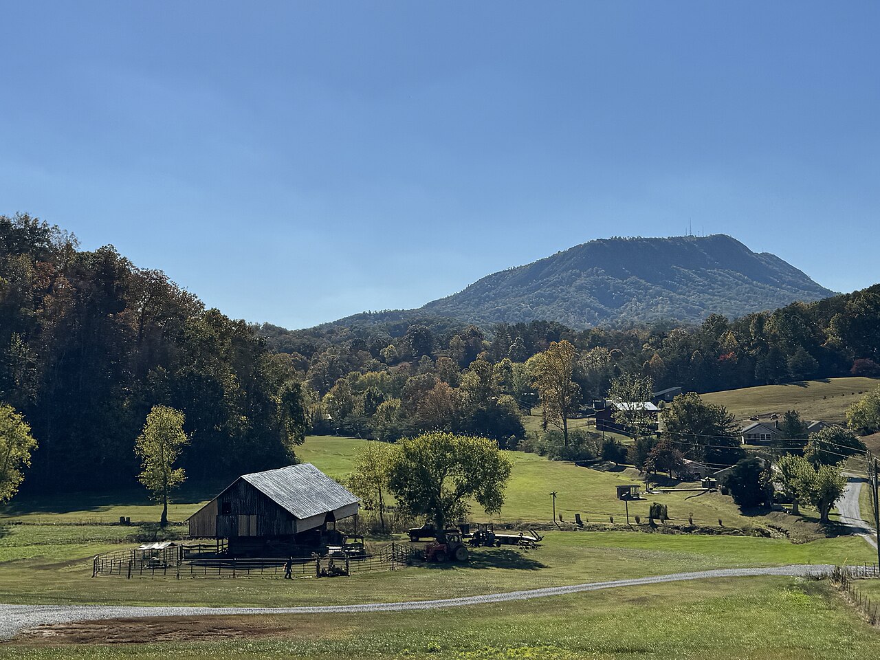 A small barn in a green valley pasture with autumn trees around it and a blue mountain ridge behind.