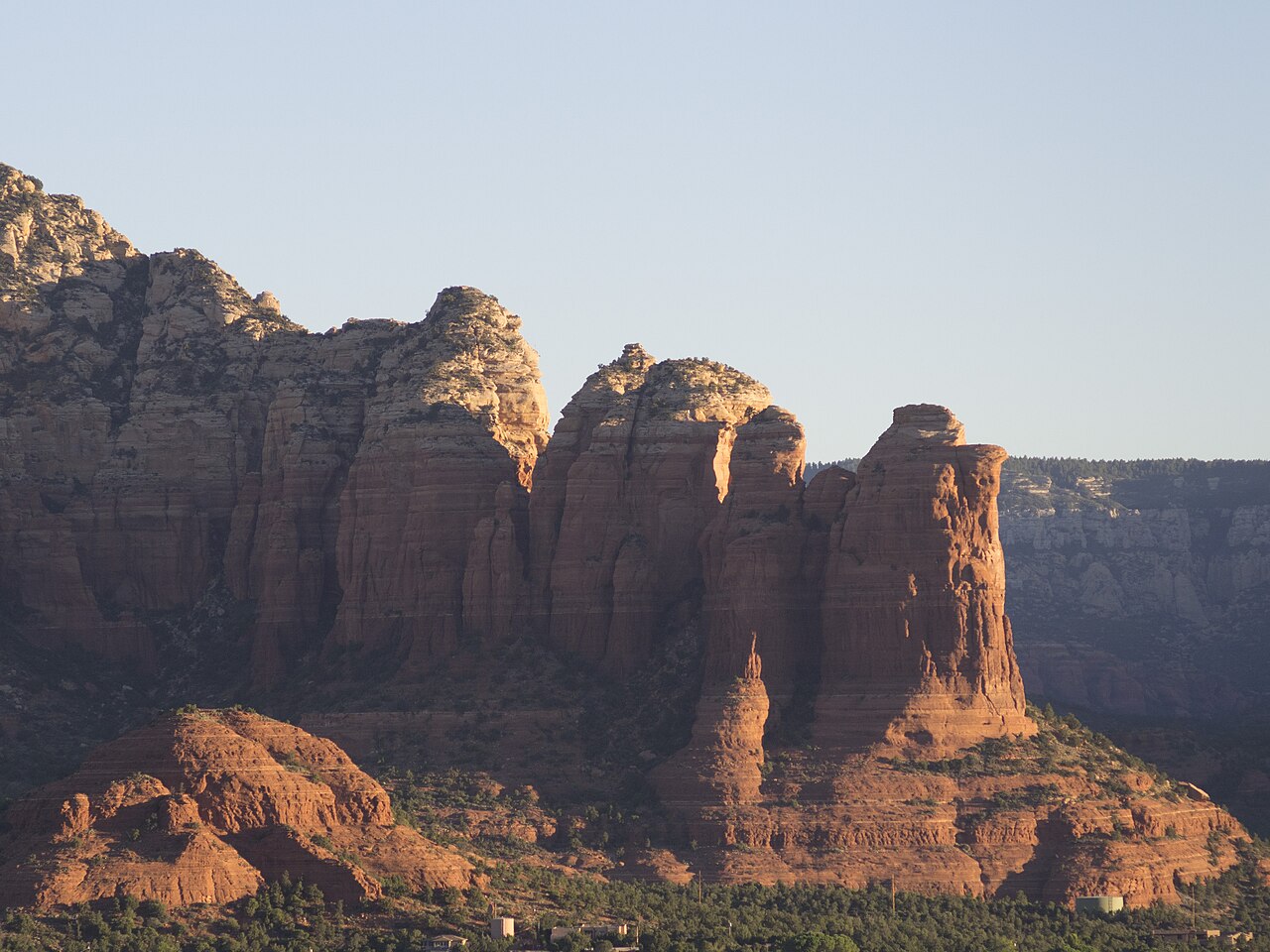 Tall red sandstone buttes and spires rising above dark green scrub in low warm light.