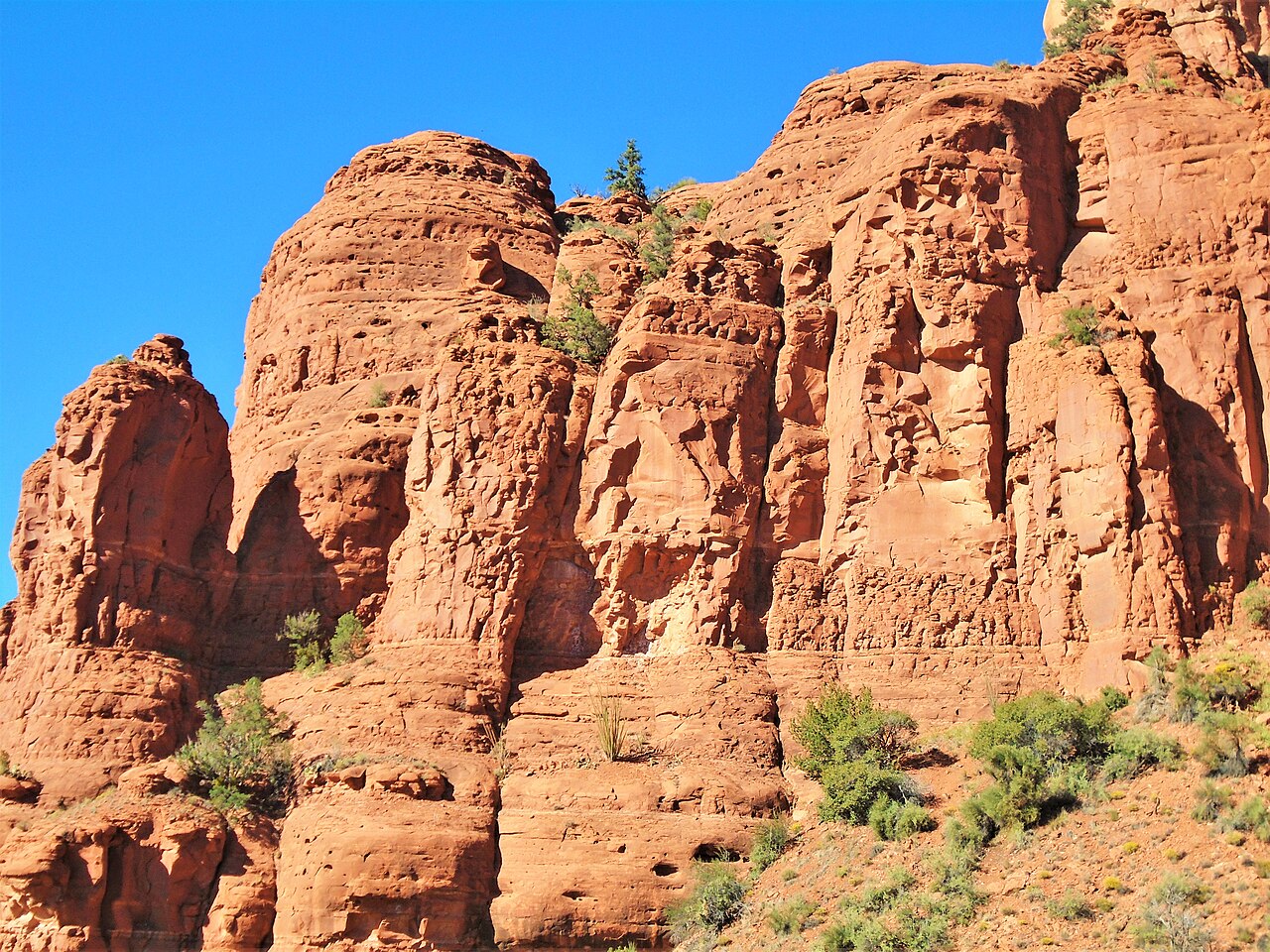 Rounded orange-red sandstone cliffs dotted with green shrubs under a deep blue sky.