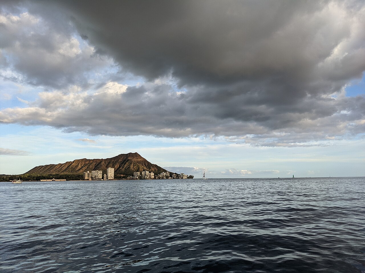 A low volcanic headland on the horizon across grey rippled sea, under heavy clouds.
