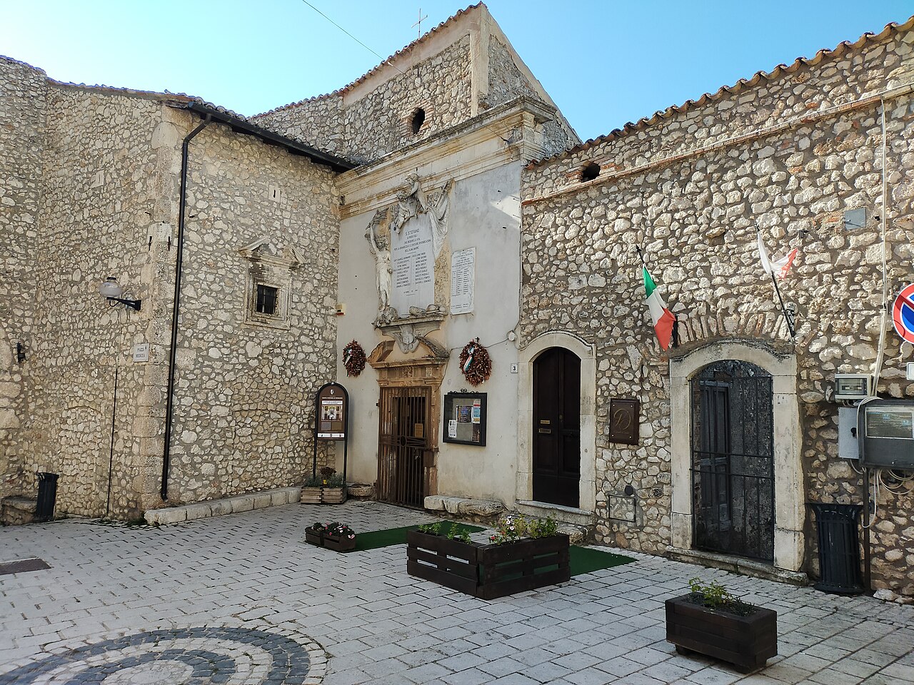 A small paved square enclosed by rough stone buildings with arched doorways and a worn church front.