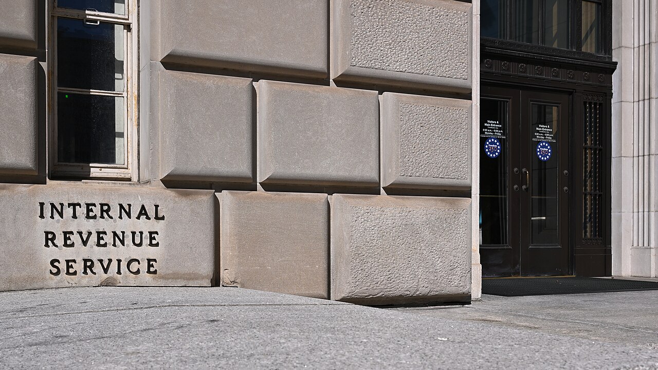A wall of large stone blocks carved with the words Internal Revenue Service beside dark double doors.