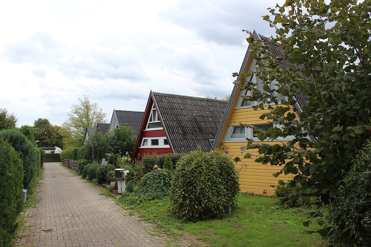 Red and yellow A-frame houses with steep dark roofs line a paved lane behind clipped hedges.