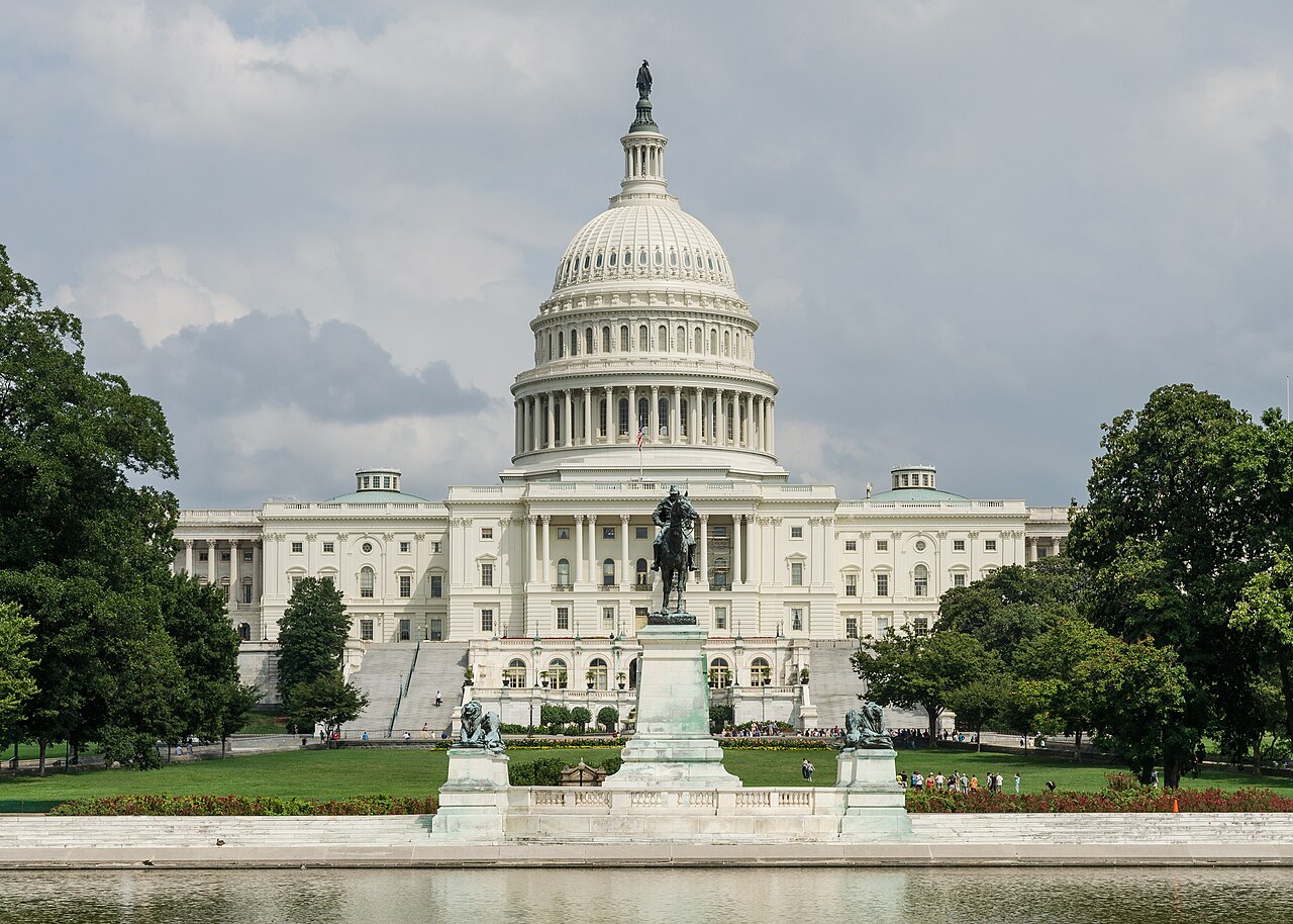A white domed building framed by trees, with a bronze equestrian statue and a reflecting pool in front, under grey cloud.