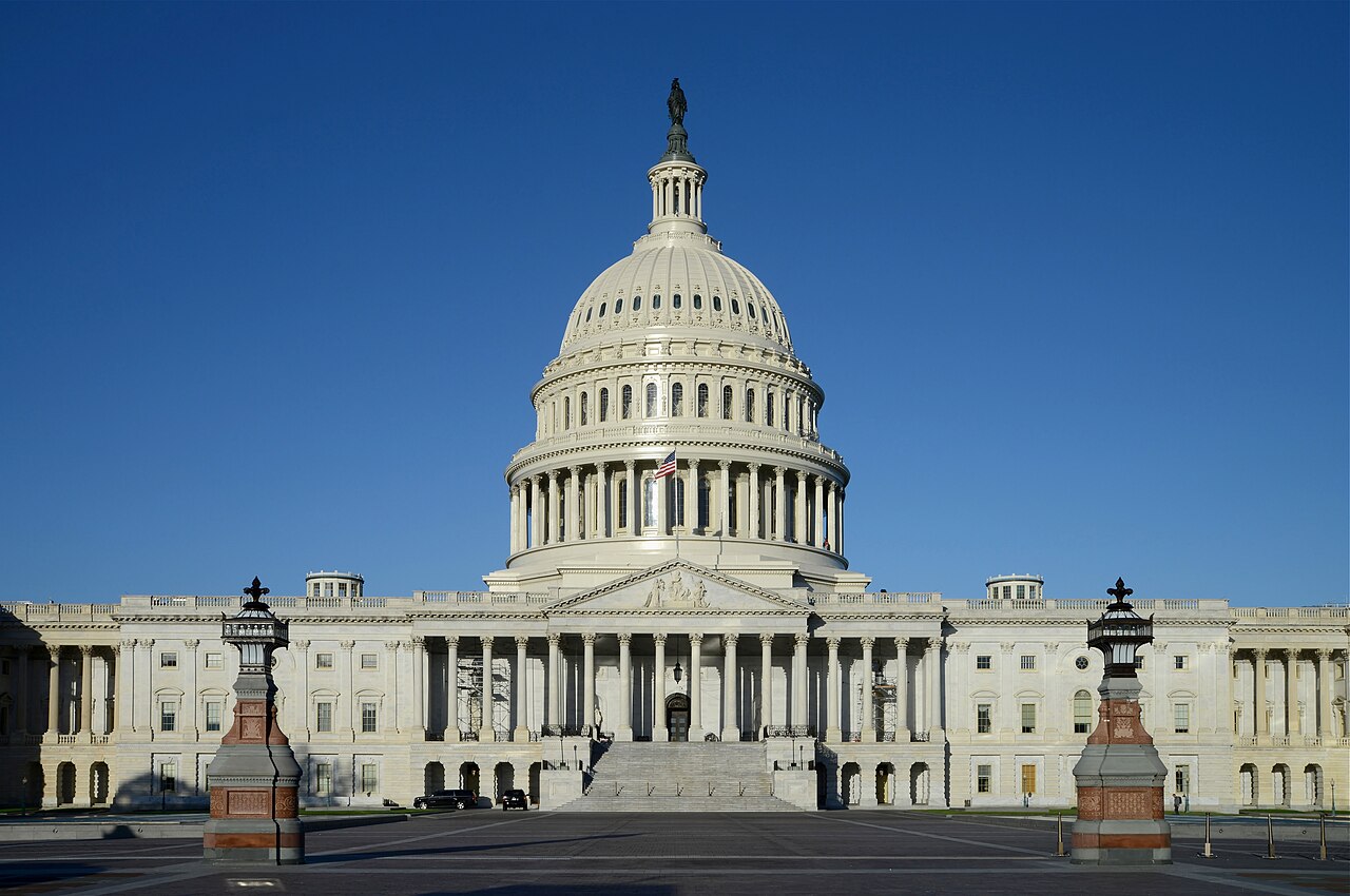 A white domed building with a columned portico and wide steps under a deep blue sky.