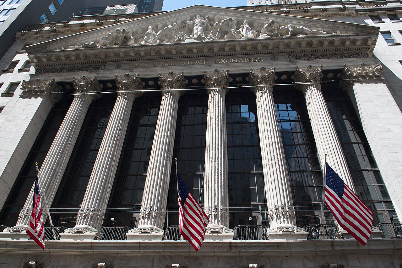 Six tall fluted stone columns under a carved pediment, with American flags hanging between them.