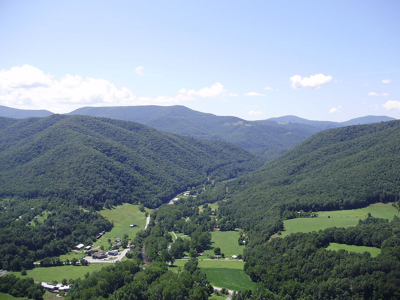 Forested mountain ridges folding down to a green valley with scattered fields and buildings.