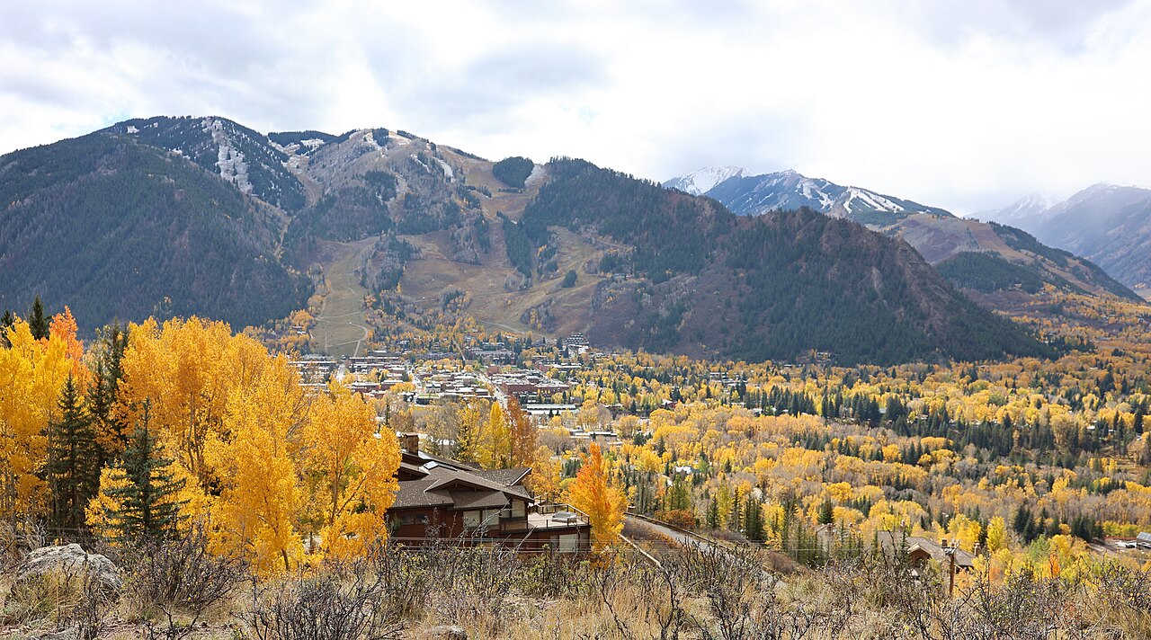 Golden aspen trees and a town in a valley below mountains streaked with ski runs.